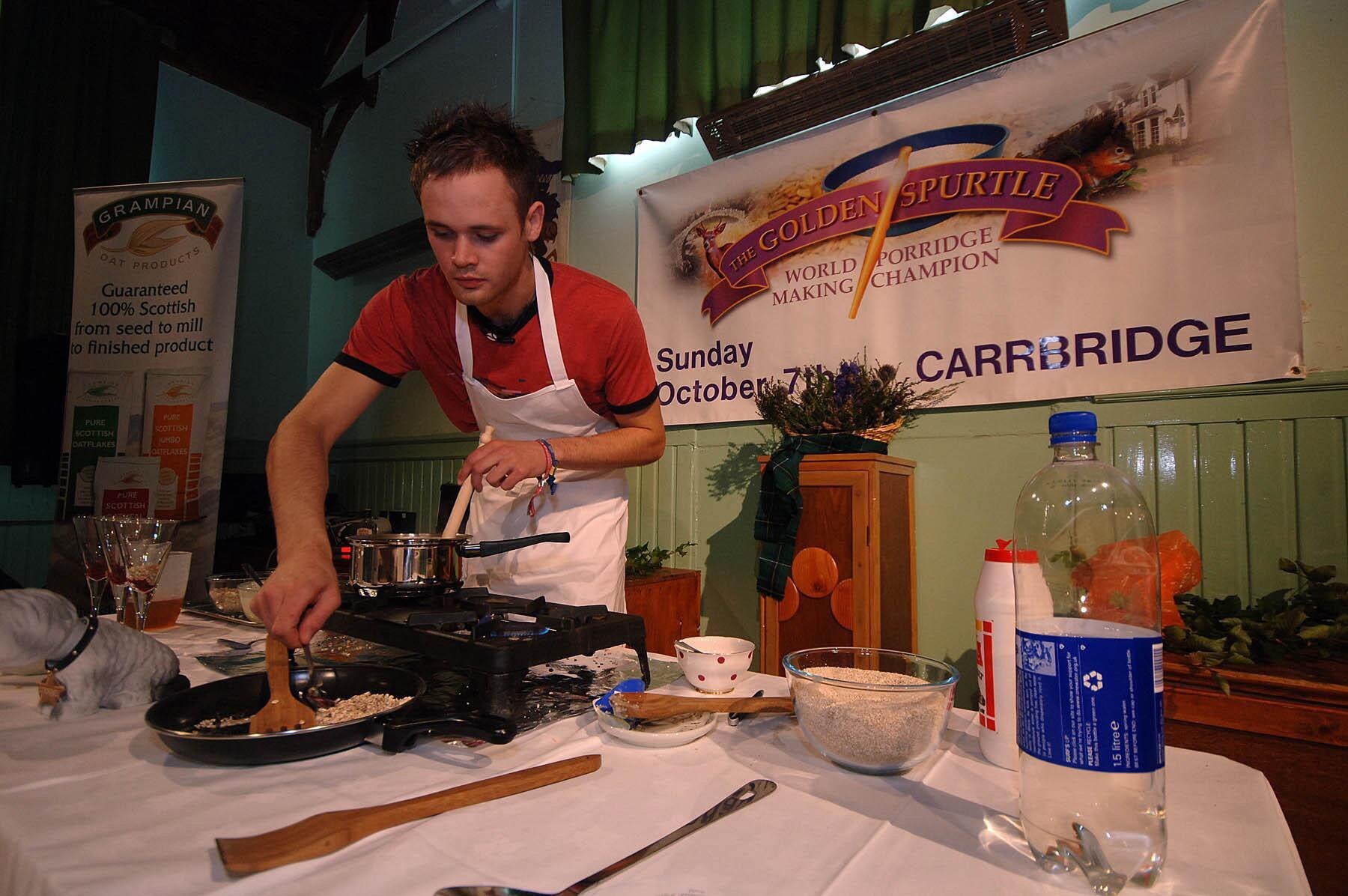 A man prepares porridge in a saucepan at a workstation in front of sign that reads 'The Golden Spurtle'.