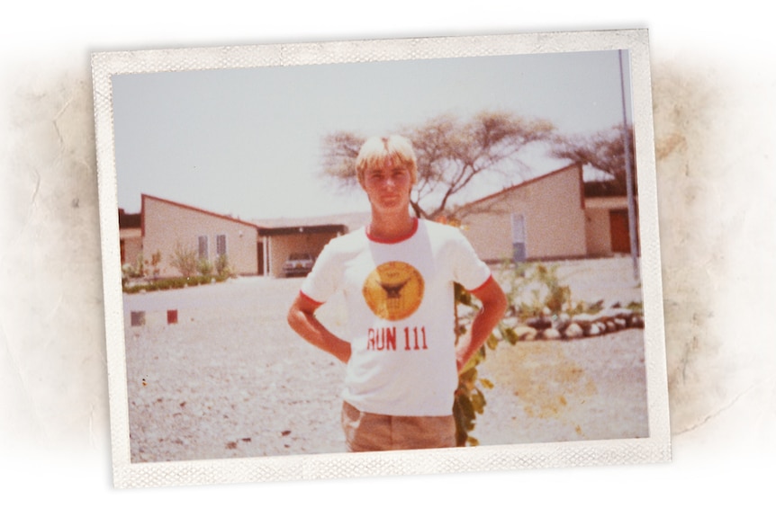 A vintage photo of a young man in a graphic t-shirt standing in a driveway.