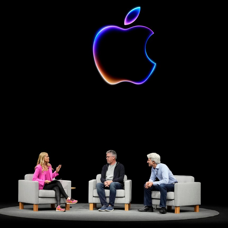 Three senior Apple staffers sitting in grey armchairs on stage at a company event