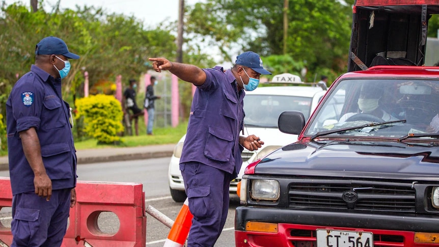 Wide shot of a uniformed man directing a driver at a checkpoint.
