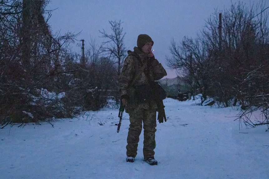 A soldier standing in snow smokes a cigarette. 