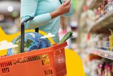 Woman holding shopping basket in aisle of supermarket with globe of Earth in basket