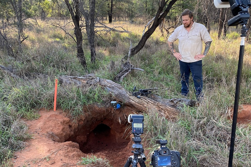 A man with his hands on his hips looks a a burrow with cameras at the front