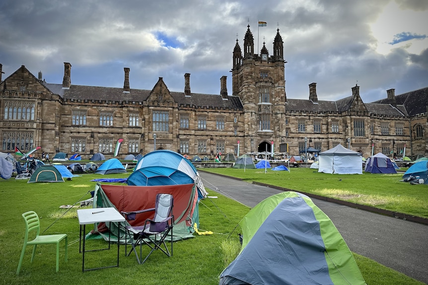 A number of tents and camping chairs on the lawn of a large university building.