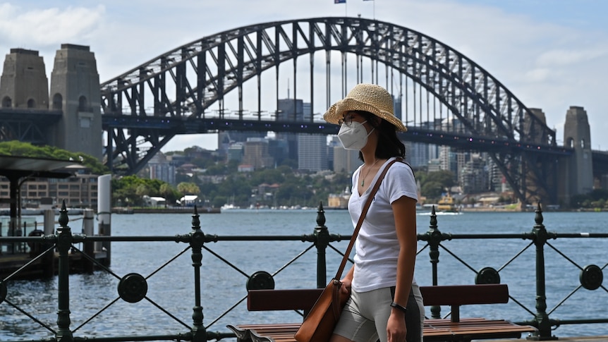 Woman walks past Sydney Harbour Bridge wearing a mask