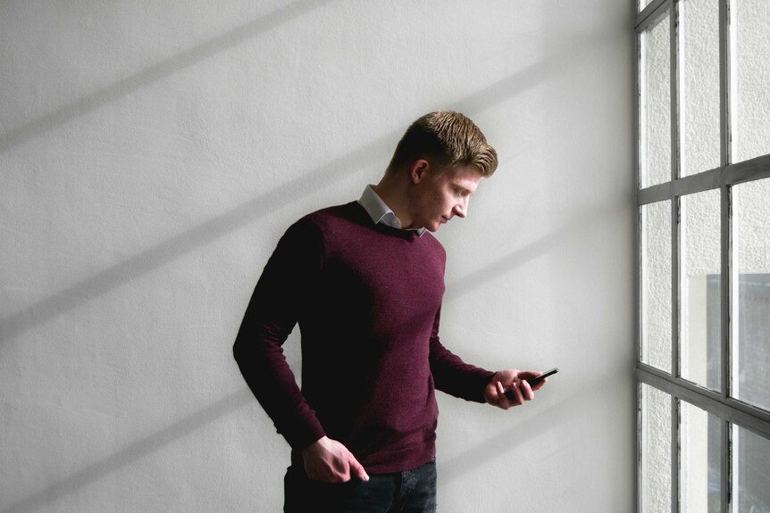 A man wearing a wool pullover looks at his phone.