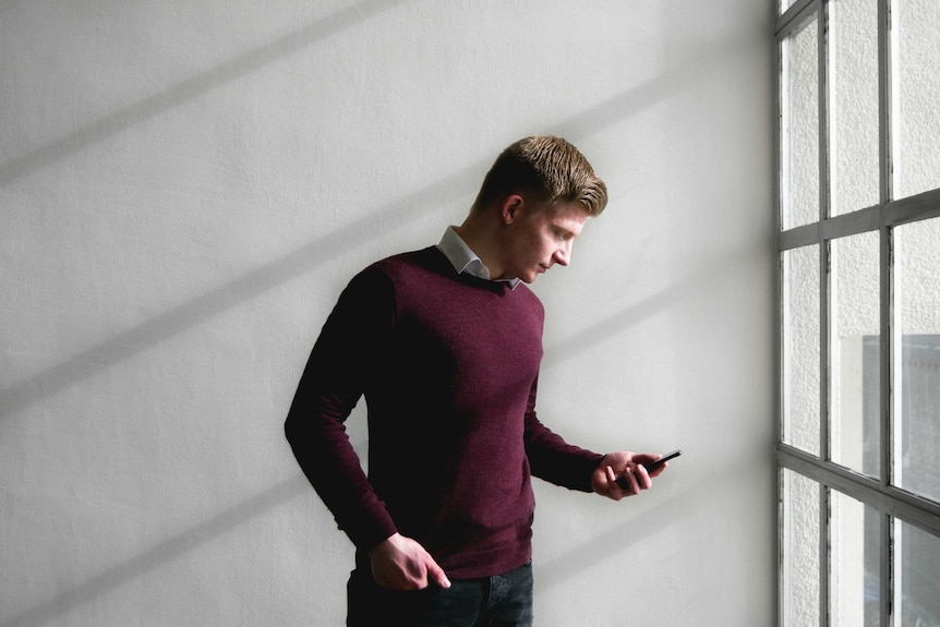 A man wearing a wool pullover looks at his phone.