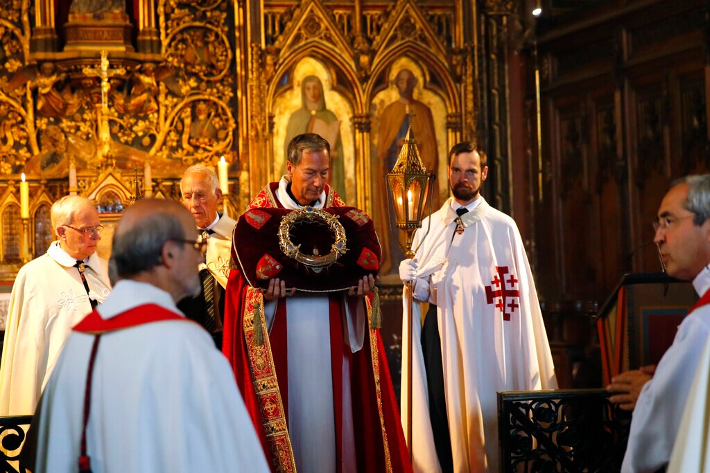 Sie sehen eine Gruppe von katholischen Priestern und kirchlichen Mitarbeitern vor einem vergoldeten Kirchenaltar, während einer eine Dornenkrone hält.