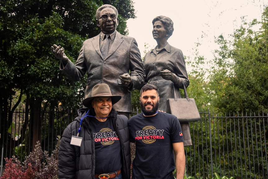 Gary Murray and Djaran Murray-Jackson pose smiling for a photo in front of a statue of Pastor Sir Doug Nicholls and Lady Gladys.