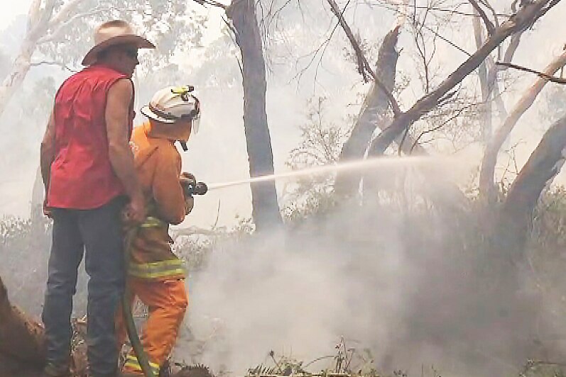 A firefighter squirts water from a hose onto burning scrubland.