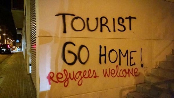 Spray paint on wall reads 'tourist go home! Refugees welcome'
