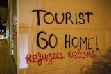Spray paint on wall reads 'tourist go home! Refugees welcome'