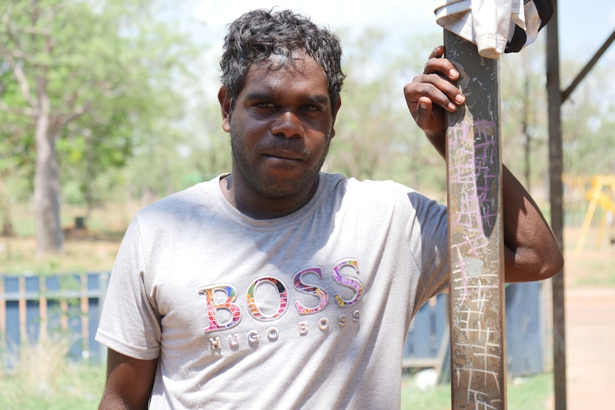 An Indigenous man leans against a pole.