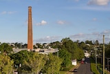 A chimney protrudes form an industrial area, which is bordred by trees