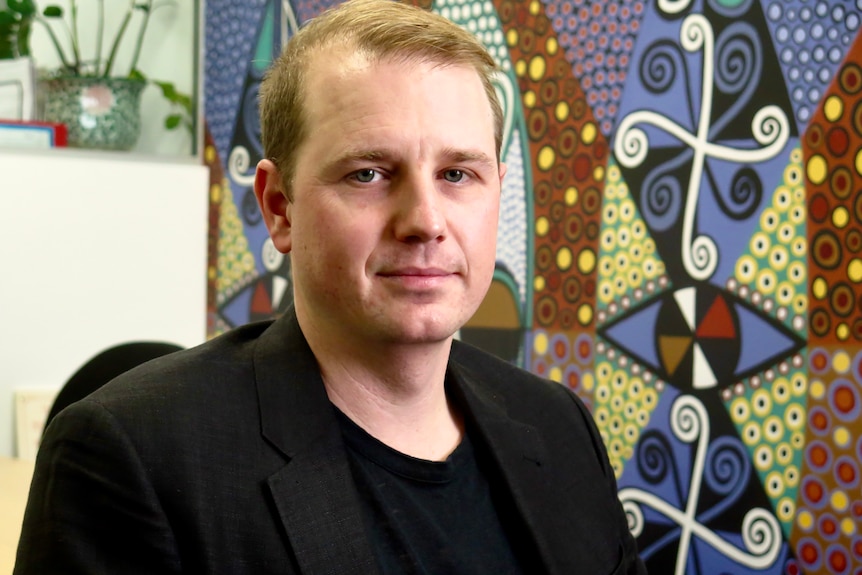 A man with short blonde hair sitting on a chair