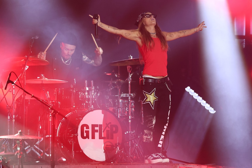 G Flip stretches her arms out as she performs in front of a drum set on stage