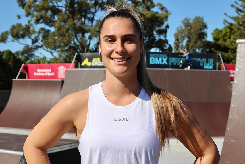 A smiling young woman stands in front of a BMX ramp.