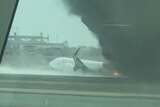 A stream of water sprays onto a plane as black smoke billows from it. 