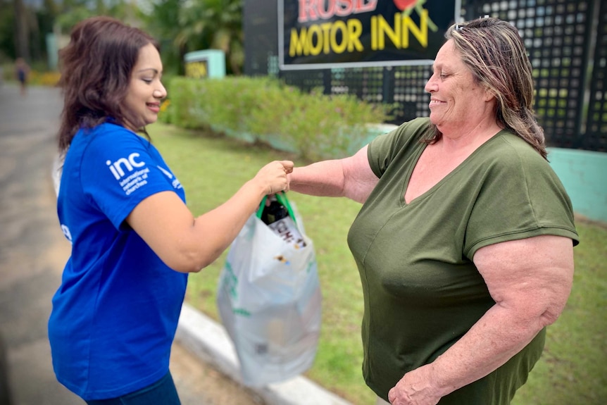 A woman hands a bag of groceries to another woman.