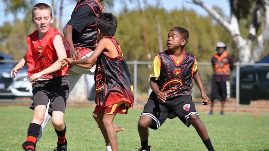 Four school-aged kids look determined as the compete in a pack for the football.