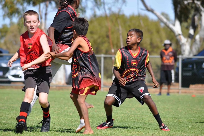 Four school-aged kids look determined as the compete in a pack for the football.