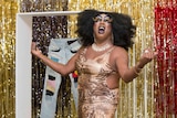 Drag queen standing in front of a tinsel curtain and jeans artwork