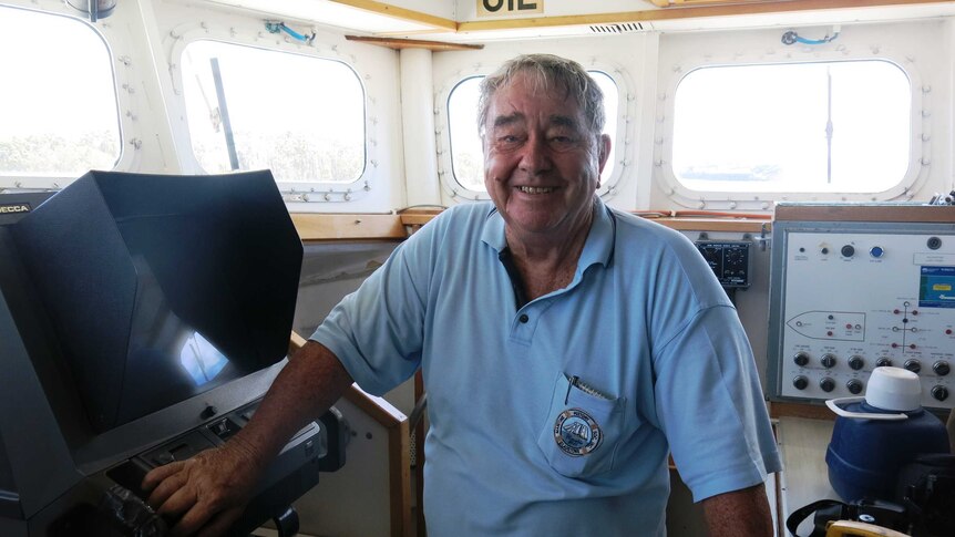 A man in a blue polo shirt in the wheelhouse of the ship looking at camera