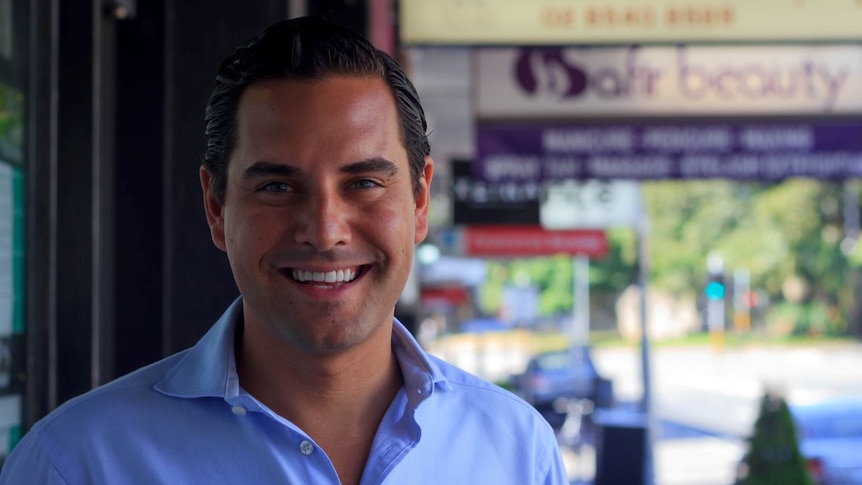 Alex Greenwich smiles with business signs in the background