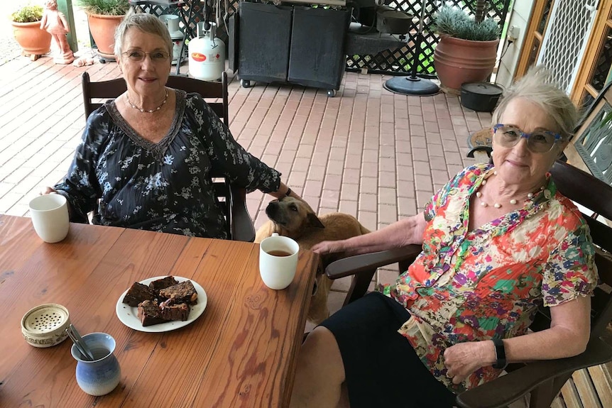 Gai Richardson and Coleen Edgar with cups of tea and a dog.