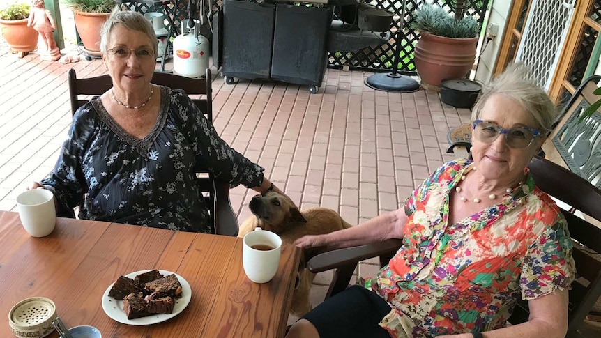 Gai Richardson and Coleen Edgar with cups of tea and a dog.