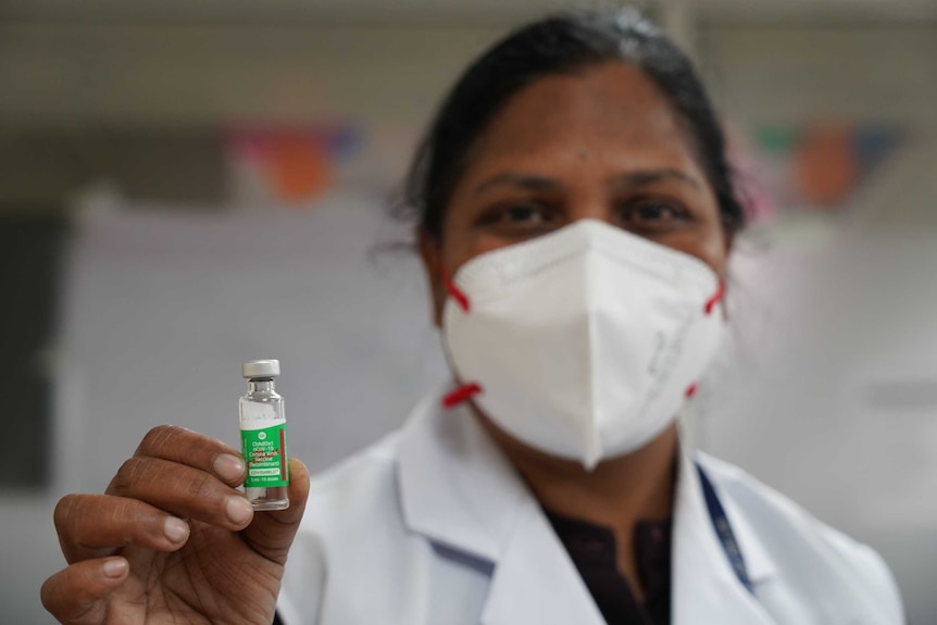 A woman in a face mask holding up a vial