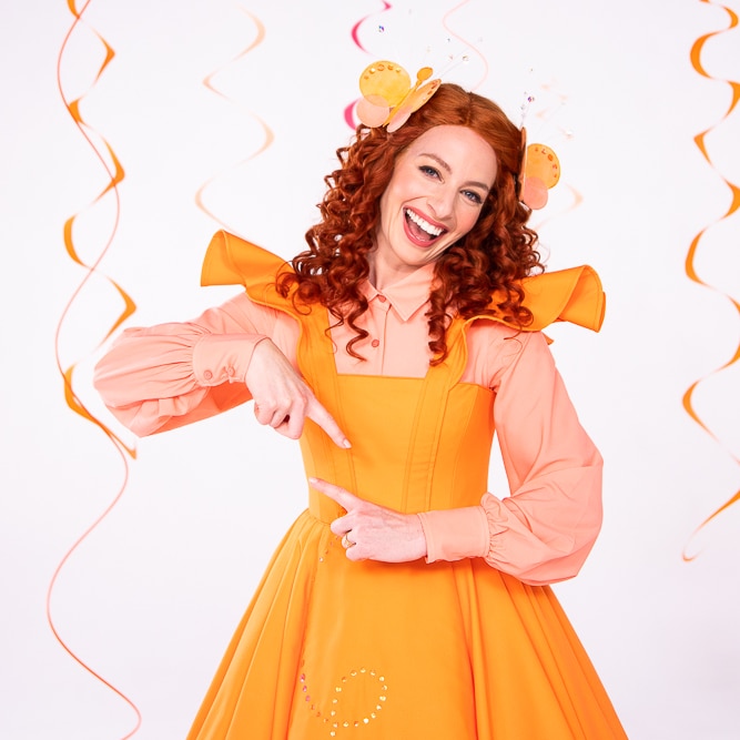 Emma Watkins in a bright orange dress performs the sign for twirl.