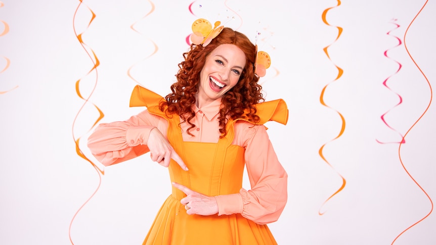 Emma Watkins in a bright orange dress performs the sign for twirl.