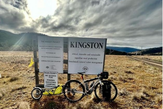 A bicycle leans against a signpost with writing on it.