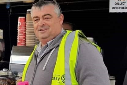 A man in a high-vis vest smiles next to a coffee machine.