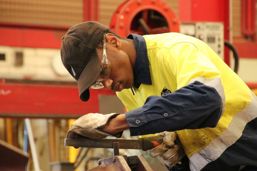 A man uses a file on a piece of metal in a workshop.