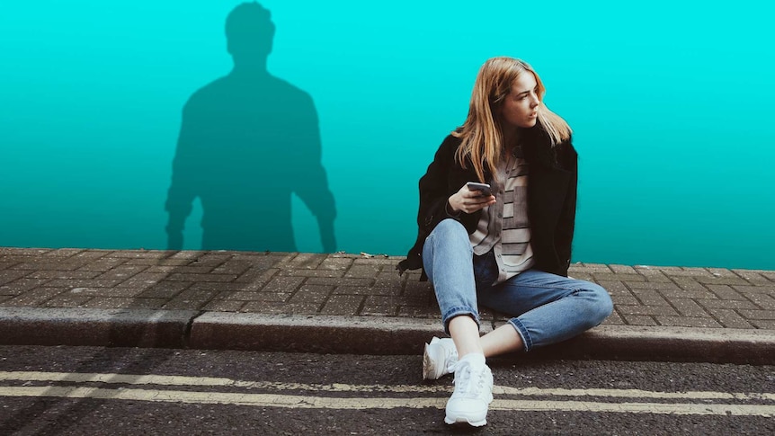 Young woman sitting down and looking around as a shadow of a stalker looms to depict what to do when you're being stalked.