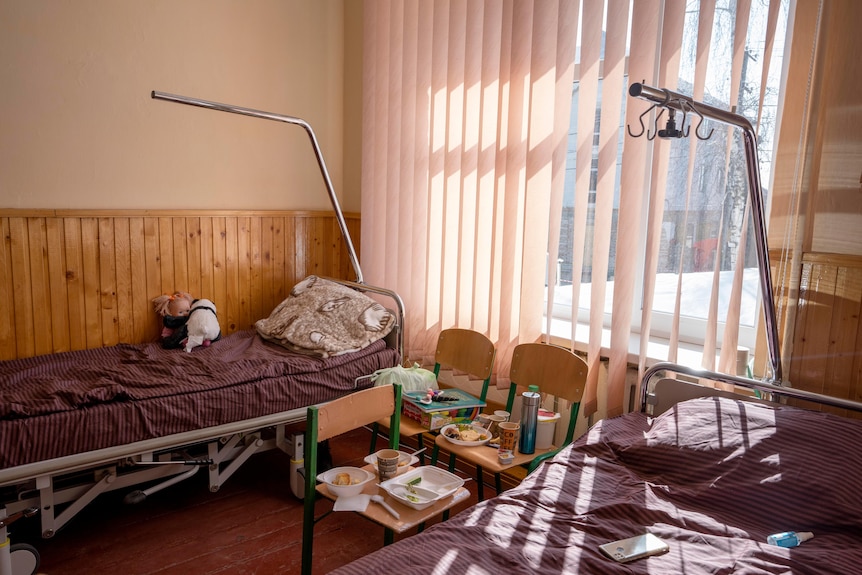 Lovos guli mokyklos name, kuris buvo paverstas lauko ligonine.  Vaikiški daiktai sėdi ant lovos. 