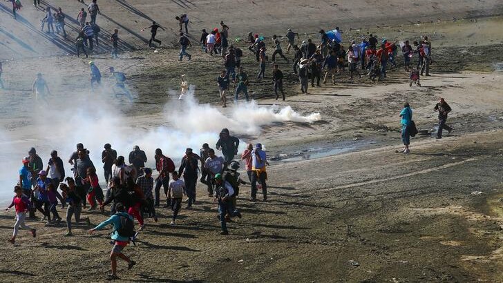 A group of migrants seen from above rush to put distance between themselves and tear gas canisters along US-Mexico border