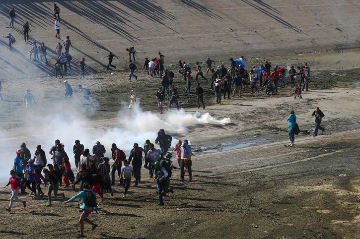 A group of migrants seen from above rush to put distance between themselves and tear gas canisters along US-Mexico border