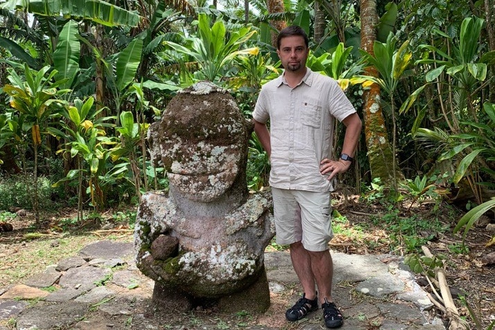 Un hombre de pie junto a una estatua de piedra tallada.