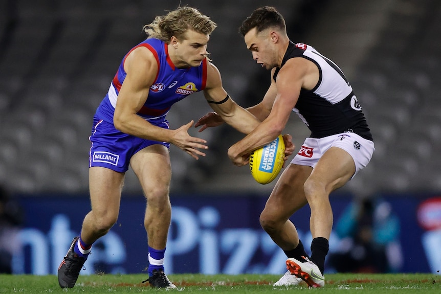 A Western Bulldogs AFL player gets his left hand to the ball at the same time as a Power opponent.