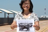 A photo of Veronica Lam standing with an archival photo near Stokes Hill Wharf in Darwin.