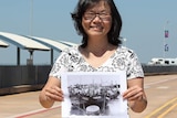 A photo of Veronica Lam standing with an archival photo near Stokes Hill Wharf in Darwin.