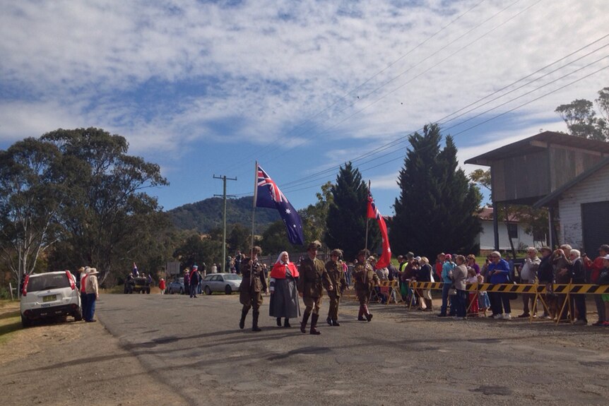 Soliders and nurses carrying flags walk down a street in Mount George with crowd watching.