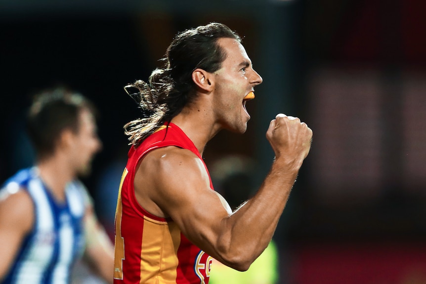 Un joueur de l'AFL des Gold Coast Suns pompe son poing droit après avoir frappé un but.