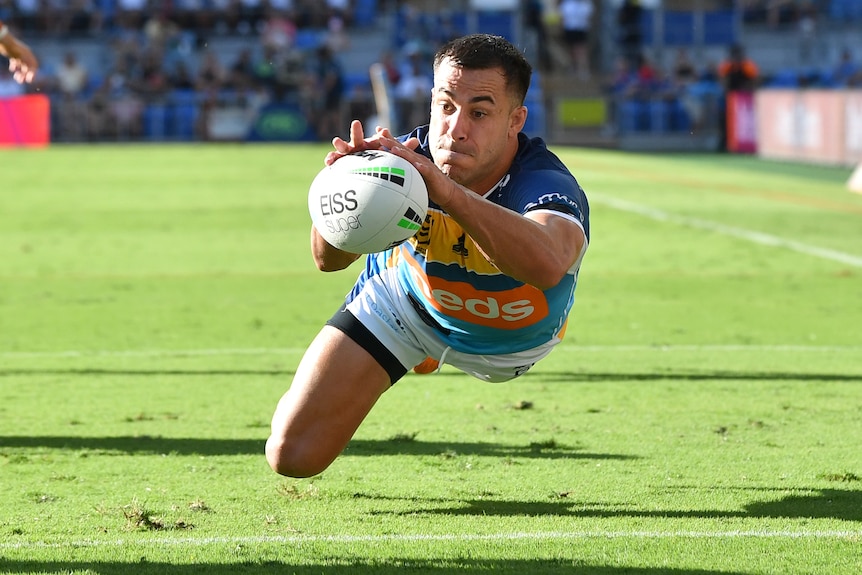 A Gold Coast Titans NRL player dives as he attempts to ground the ball for a try.