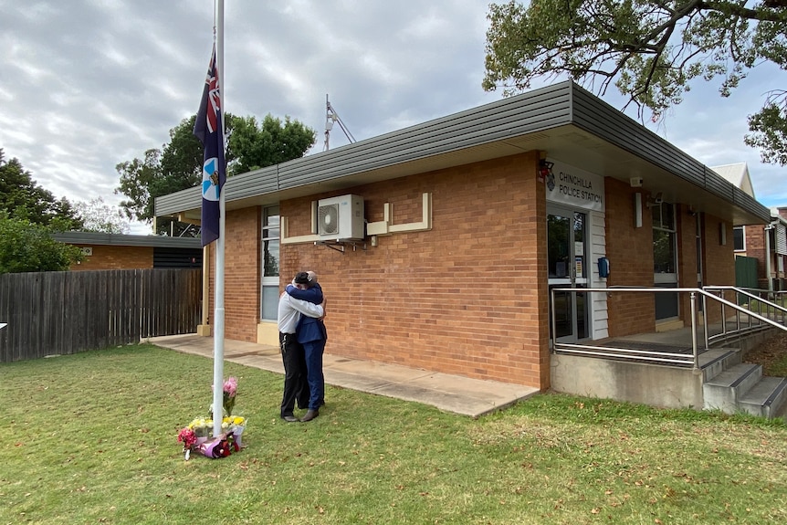 Local residents hug by the flagpole at Chinchilla police station after the death of two officers during a siege at Wieambilla.