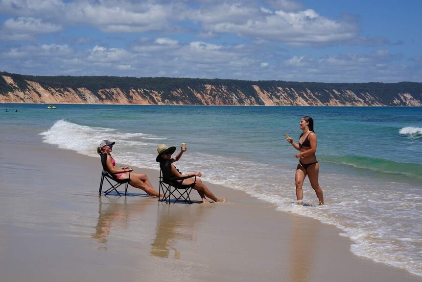 School leavers sits in chairs in the surf with a drink at Rainbow Beach on Queensland's Sunshine Coast.