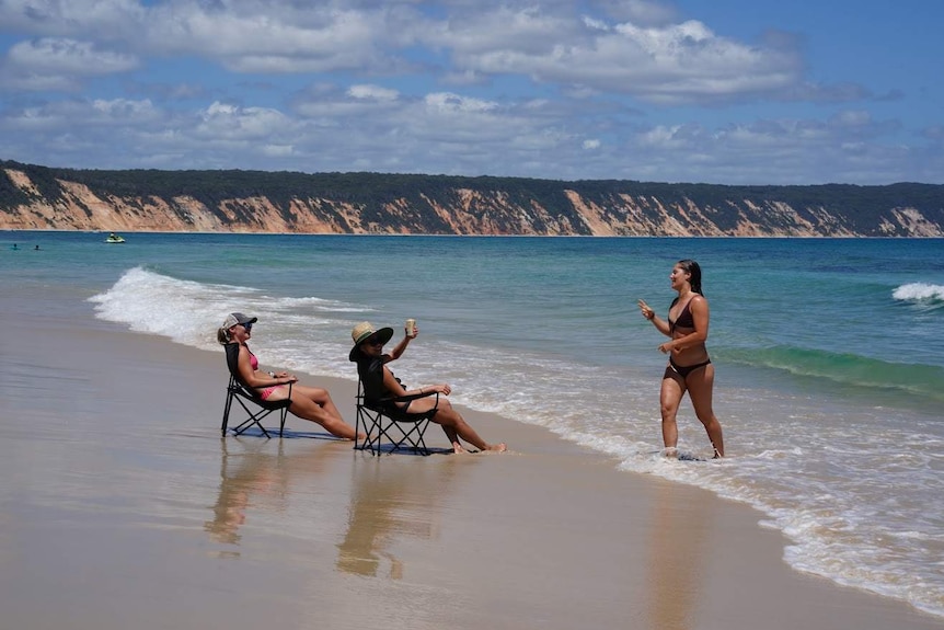 School leavers sits in chairs in the surf with a drink at Rainbow Beach on Queensland's Sunshine Coast.